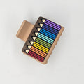 Hand-painted rainbow of colored pencils fanned diagonally with engraved natural wood tips on dark-stained wood, attached to a 2-inch matte tan claw clip