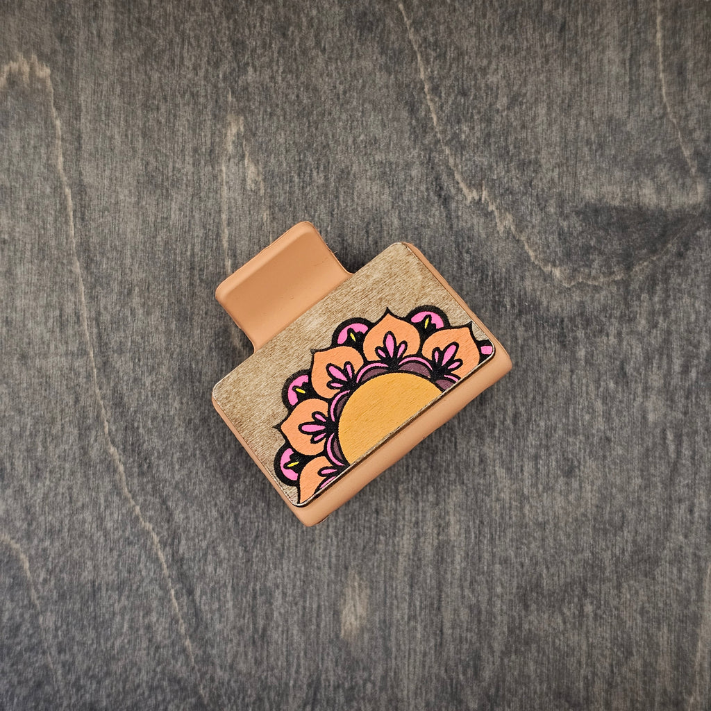 Hand-painted half-mandala in burnt orange and hot pink with yellow accents on natural walnut wood grain, attached to a 2-inch matte copper terracotta claw clip