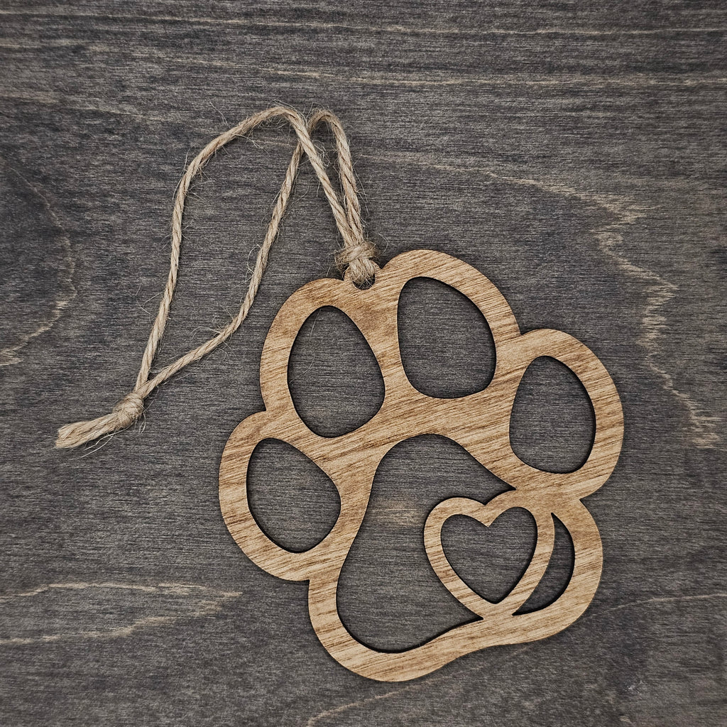 Laser cut wood paw print ornament with open silhouette design and heart cutout in the lower pad, hung with natural jute cord