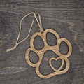 Laser cut wood paw print ornament with open silhouette design and heart cutout in the lower pad, hung with natural jute cord