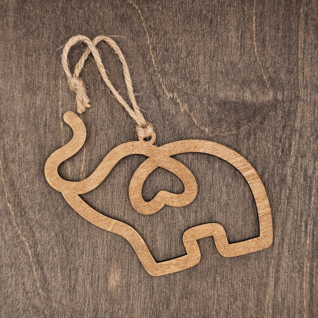 Laser cut wood elephant ornament formed from a single continuous flowing line with a heart detail in the body, hung with natural jute cord