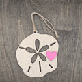 Laser cut wood sand dollar ornament with five-petal cutout and hand-painted pink heart accent, hung with natural jute cord