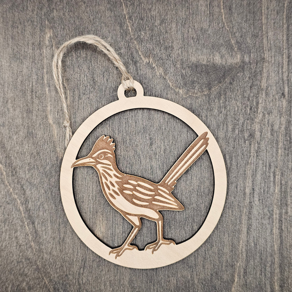 Laser cut and engraved Greater Roadrunner wood ornament, featuring an open silhouette design with detailed feather engraving inside a circular wood frame, hung with natural jute cord