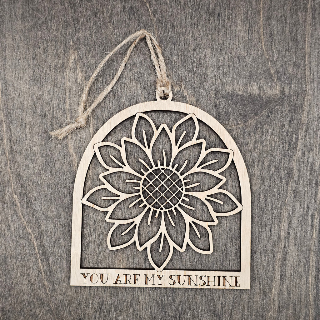 Laser cut wood sunflower ornament in an arched frame with detailed petal and seed head cutwork, "You Are My Sunshine" engraved at the base, hung with natural jute cord