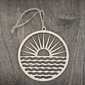 Laser cut wood sunrise ornament with radiating sun rays and rolling waves inside a circular frame, hung with natural jute cord