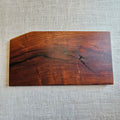 A rectangular wooden serving board with a natural live edge and prominent wood grain, displayed on a textured light gray linen background.