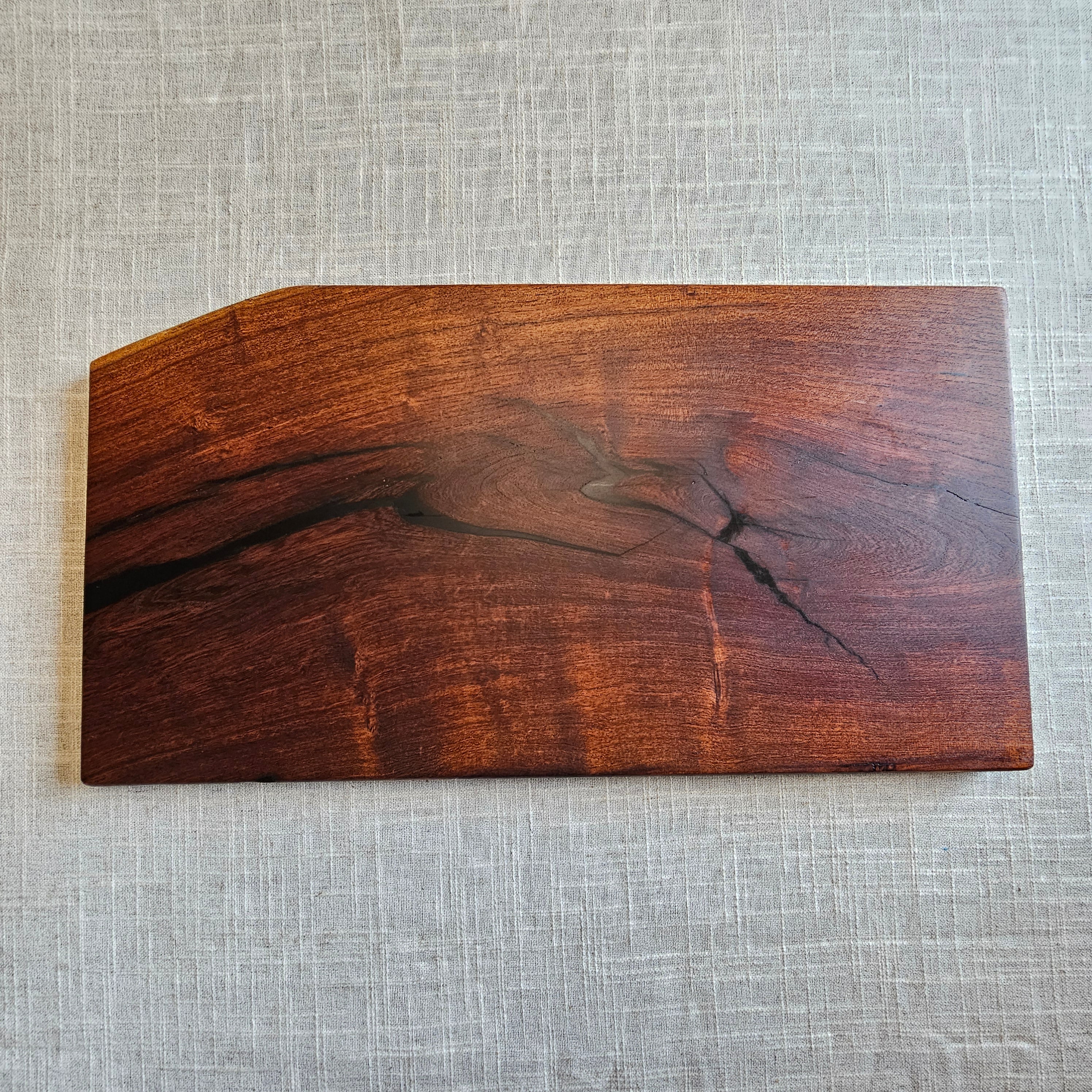 A rectangular wooden serving board with a natural live edge and prominent wood grain, displayed on a textured light gray linen background.