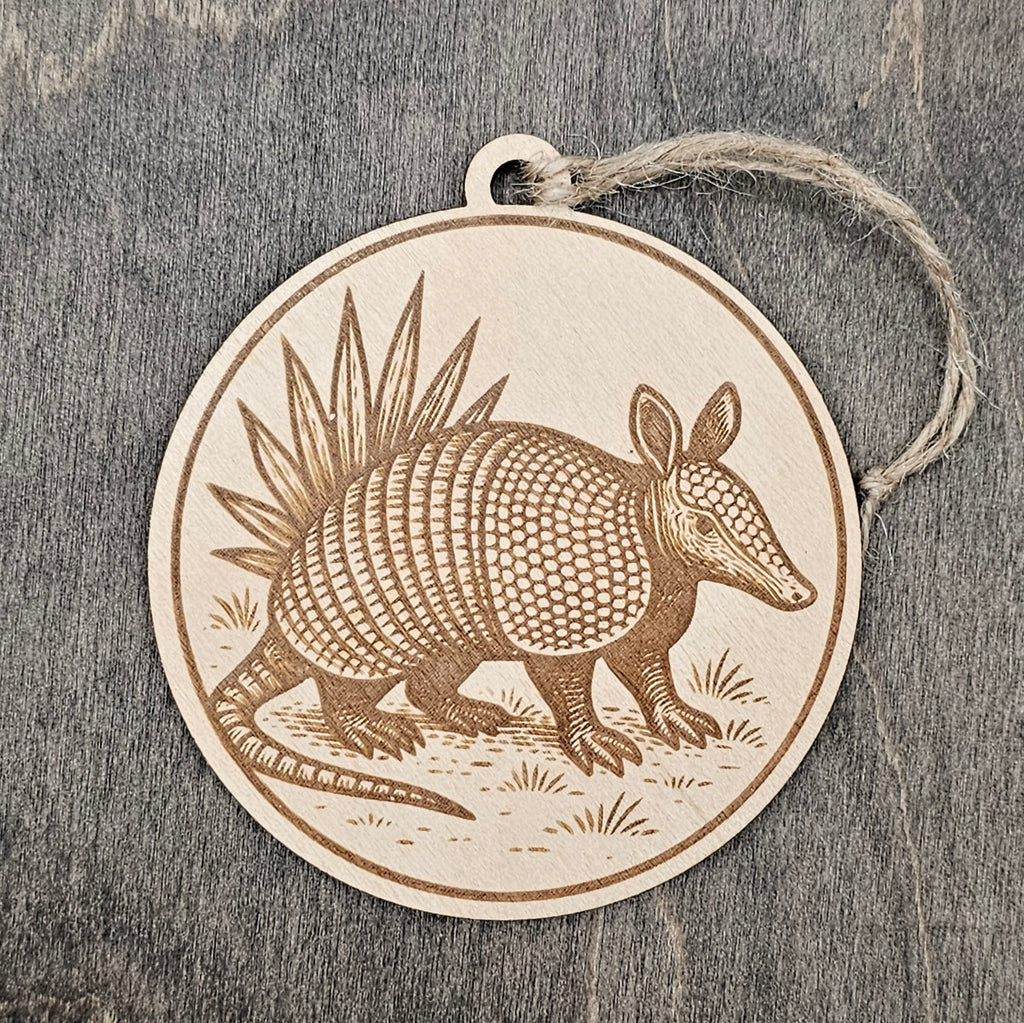 Laser engraved Armadillo wood ornament, featuring a detailed illustration of this Texas icon with its banded shell, walking through native grassland with yucca in the background, hung with natural jute cord