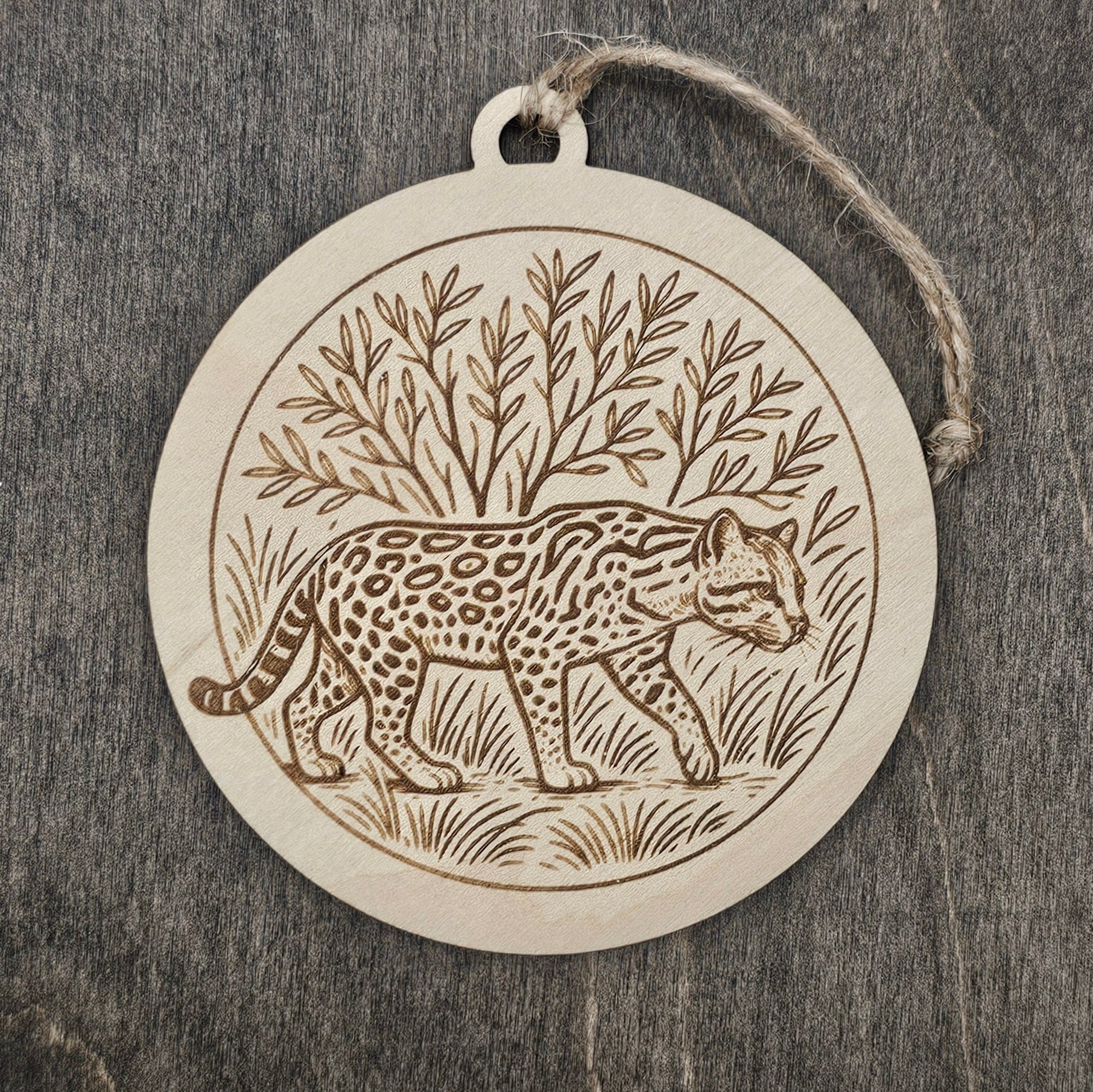Laser engraved Ocelot wood ornament, featuring a detailed illustration of this rare South Texas wild cat walking through native brushland, hung with natural jute cord