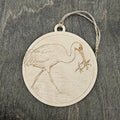 Laser engraved Whooping Crane wood ornament, featuring a detailed illustration of this endangered bird wading in coastal marsh waters with a blue crab, hung with natural jute cord