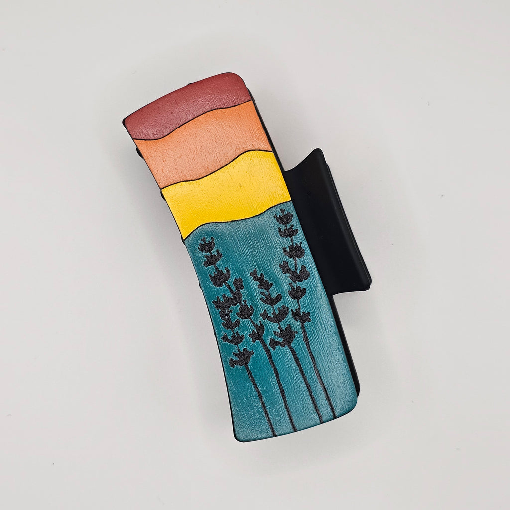 Hand-painted wood hair claw clip featuring a prairie sunset scene with wildflower silhouettes in teal, yellow, and red tones