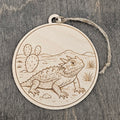 Laser engraved Texas Horned Lizard wood ornament, featuring a detailed illustration of this beloved Texas icon against a West Texas landscape with prickly pear cactus and mountains, hung with natural jute cord