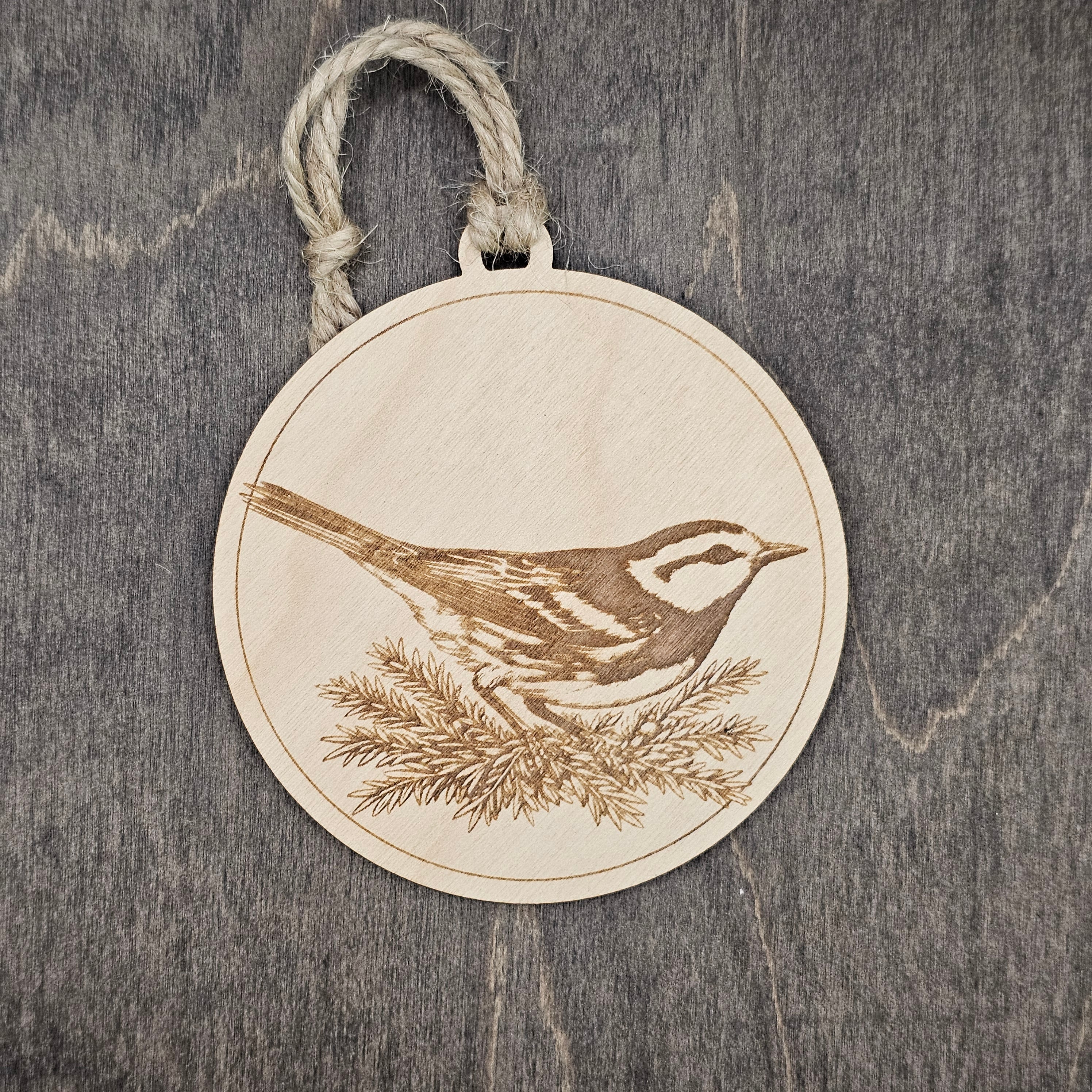 Laser engraved Golden-cheeked Warbler wood ornament, featuring a detailed illustration of this endangered Texas songbird nestled among juniper foliage, hung with natural jute cord