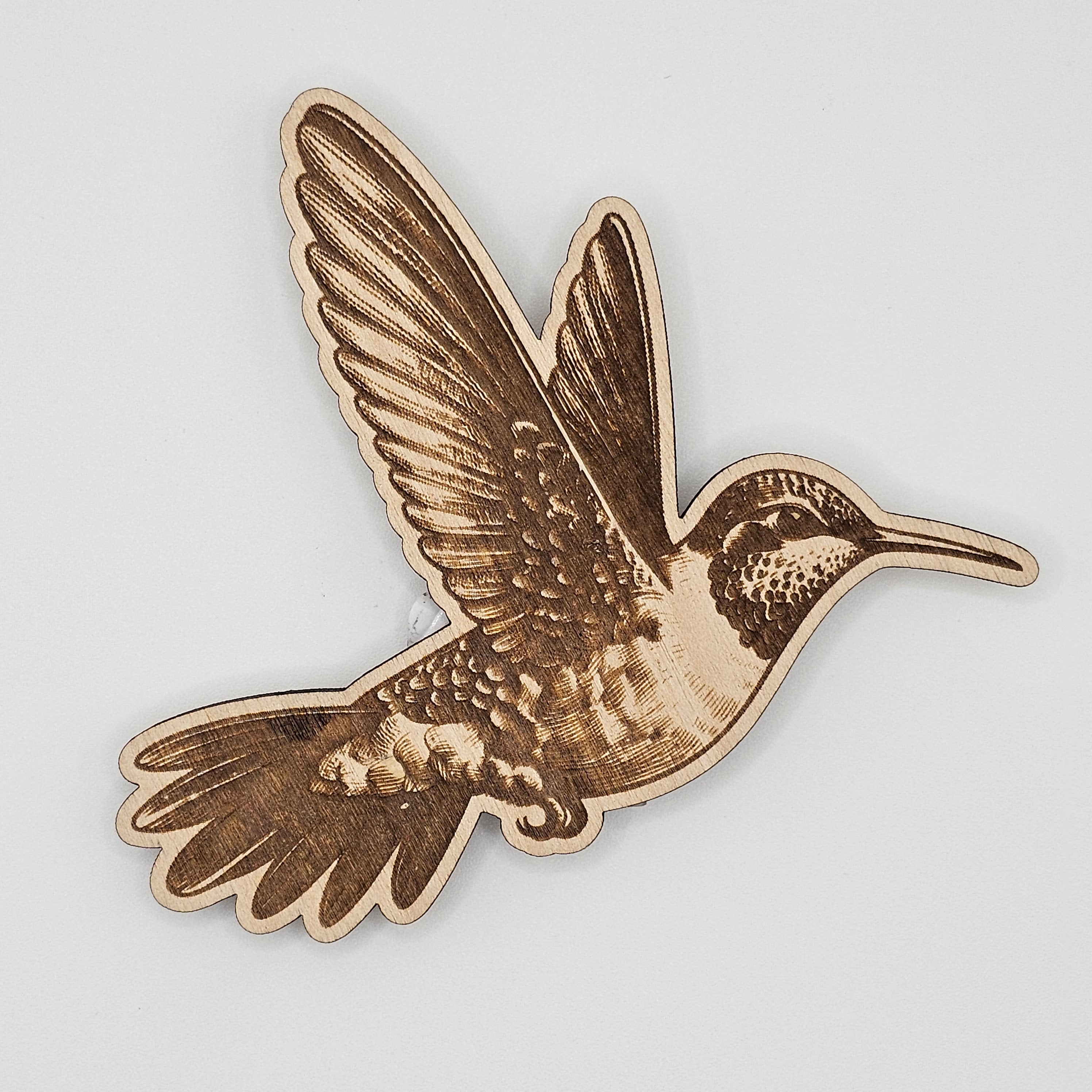 Laser-engraved wood magnet shaped like a hummingbird in flight with detailed feather engraving